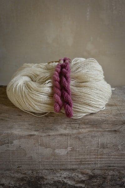 Sur une planche en bois, un écheveau de laine blanc et deux échevettes de laine roses teintes naturellement avec du bois rouge