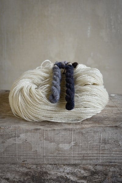 Sur une planche en bois, un écheveau de laine blanc et deux échevettes de laine bleues teintes naturellement avec du campêche