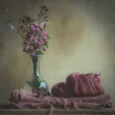 un écheveau de laine et une étole de lin teints en rose avec des plantes uniquement accompagné d'un bouquet de petites roses